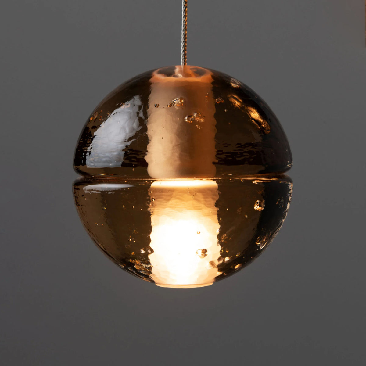 Bocci 14.20 Random by Omer Arbel. A gleaming copper sphere pendant glows warmly against gray.