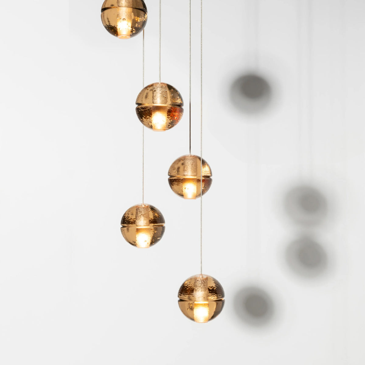 Bocci 14.5 Random by Omer Arbel. Five golden spherical pendants hang vertically, casting warm glowing light and shadows.