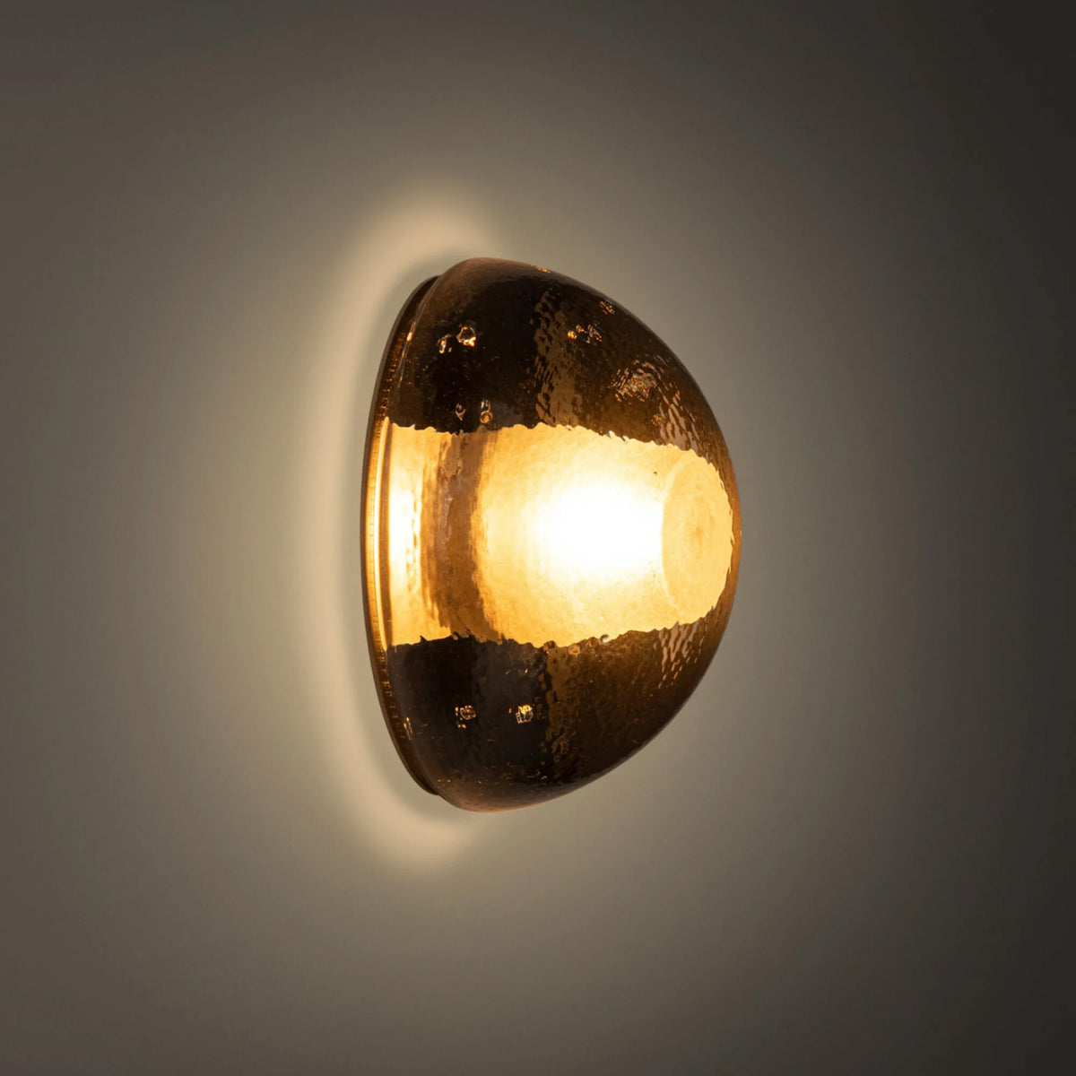 Bocci 14s Wall and Ceiling Lamp by Omer Arbel. A brass egg-shaped wall light glows warmly against a neutral background.