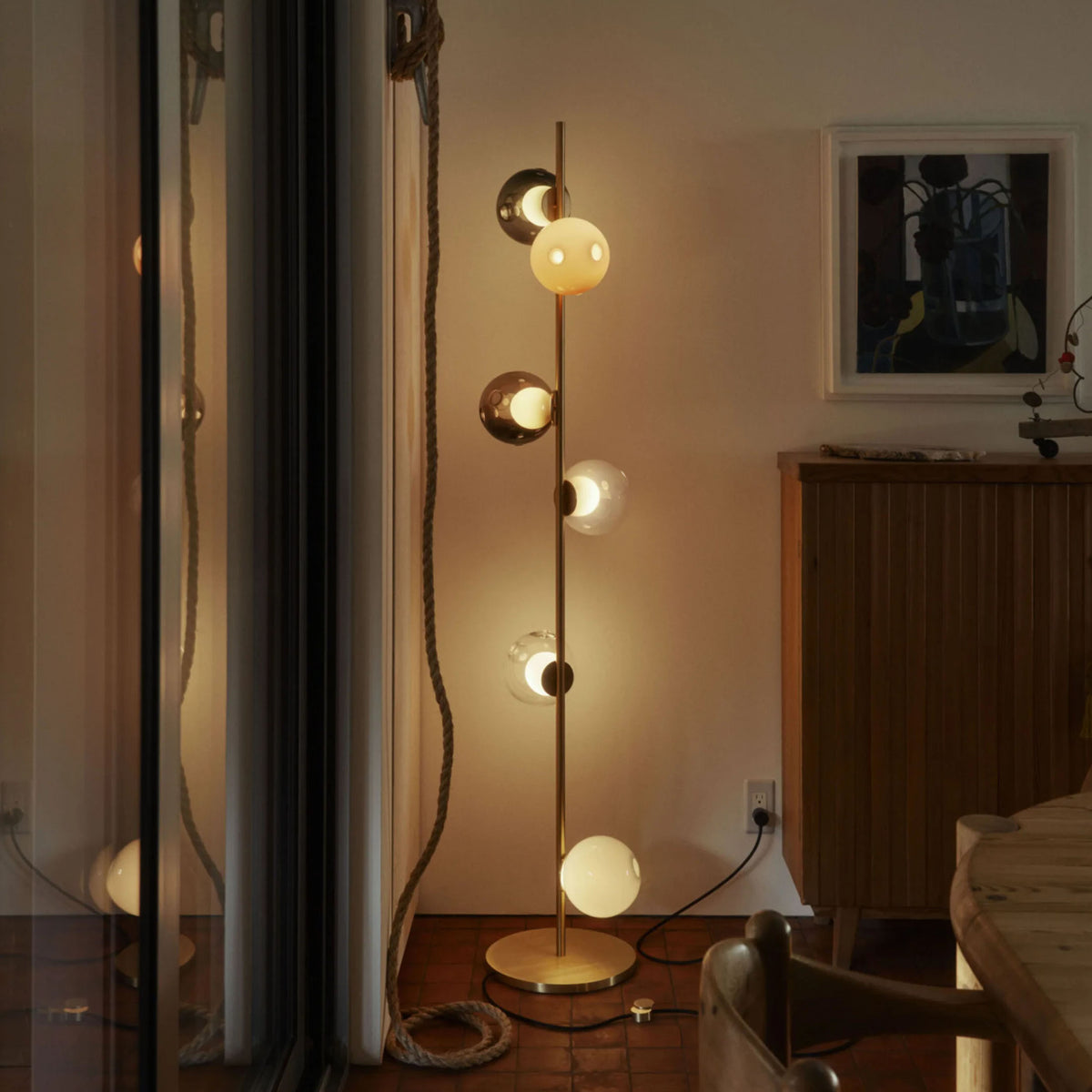 Bocci 28.6 Stem Floor by Omer Arbel. A brass floor lamp with glowing spherical shades illuminates a cozy interior space.