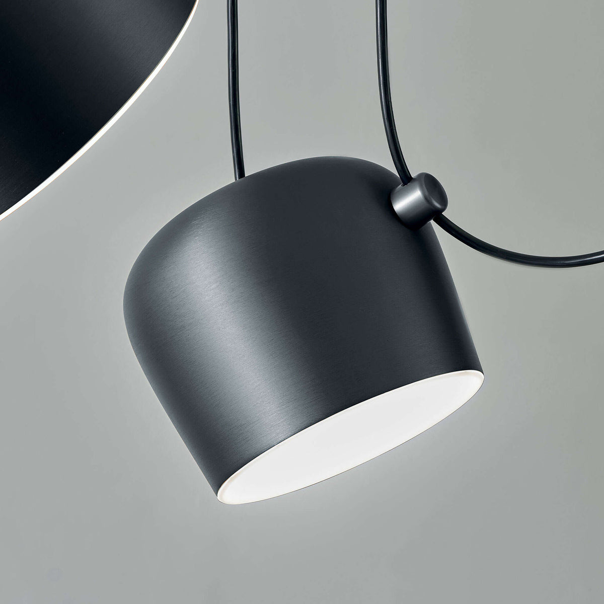 Flos Aim Suspension Lamps by Erwan & Ronan Bouroullec. A sleek black pendant lamp with white interior glows softly.