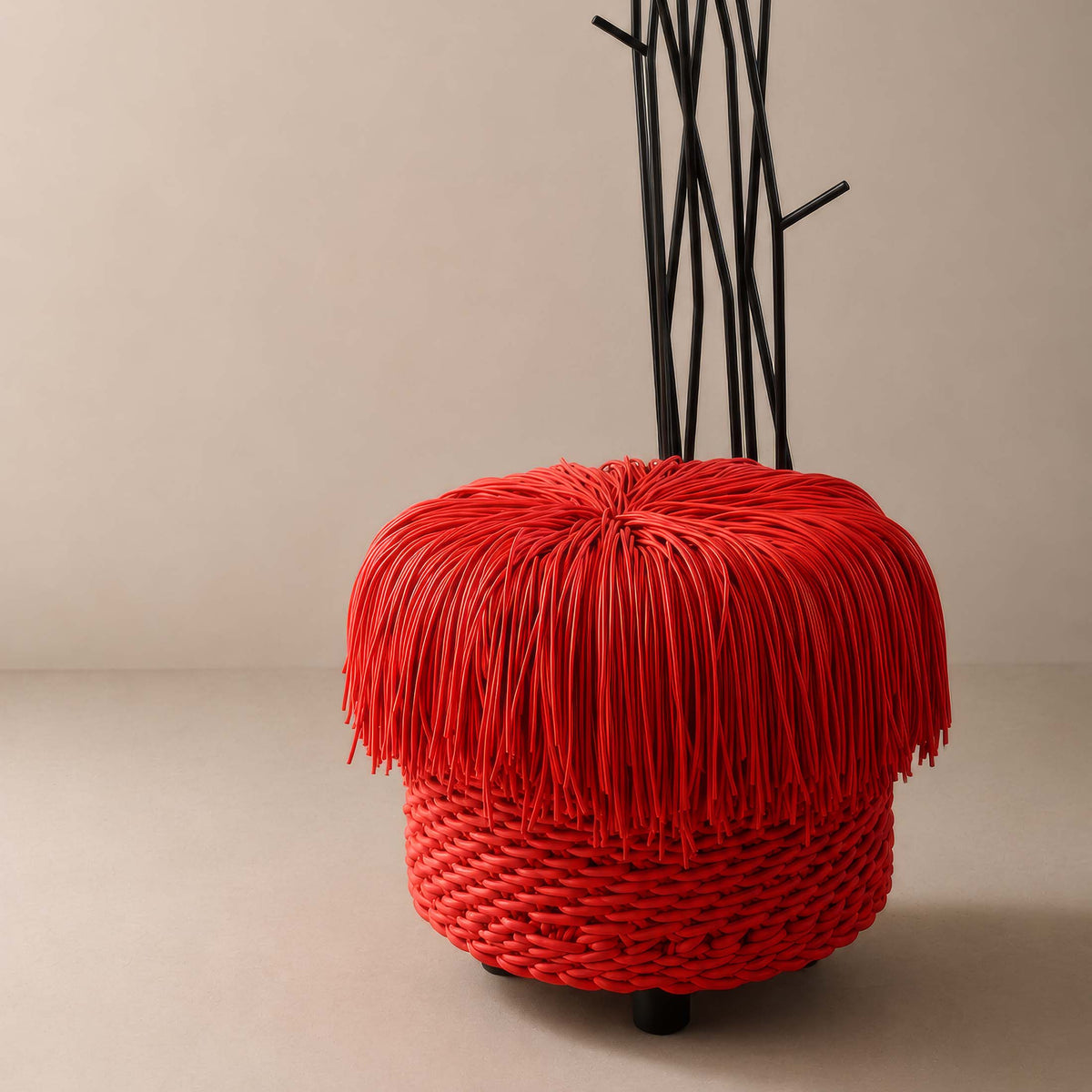 COVO Anemon Pouf by Rosanna Contadini. A vibrant red woven sphere with black wire stems emerges from a neutral gallery floor.