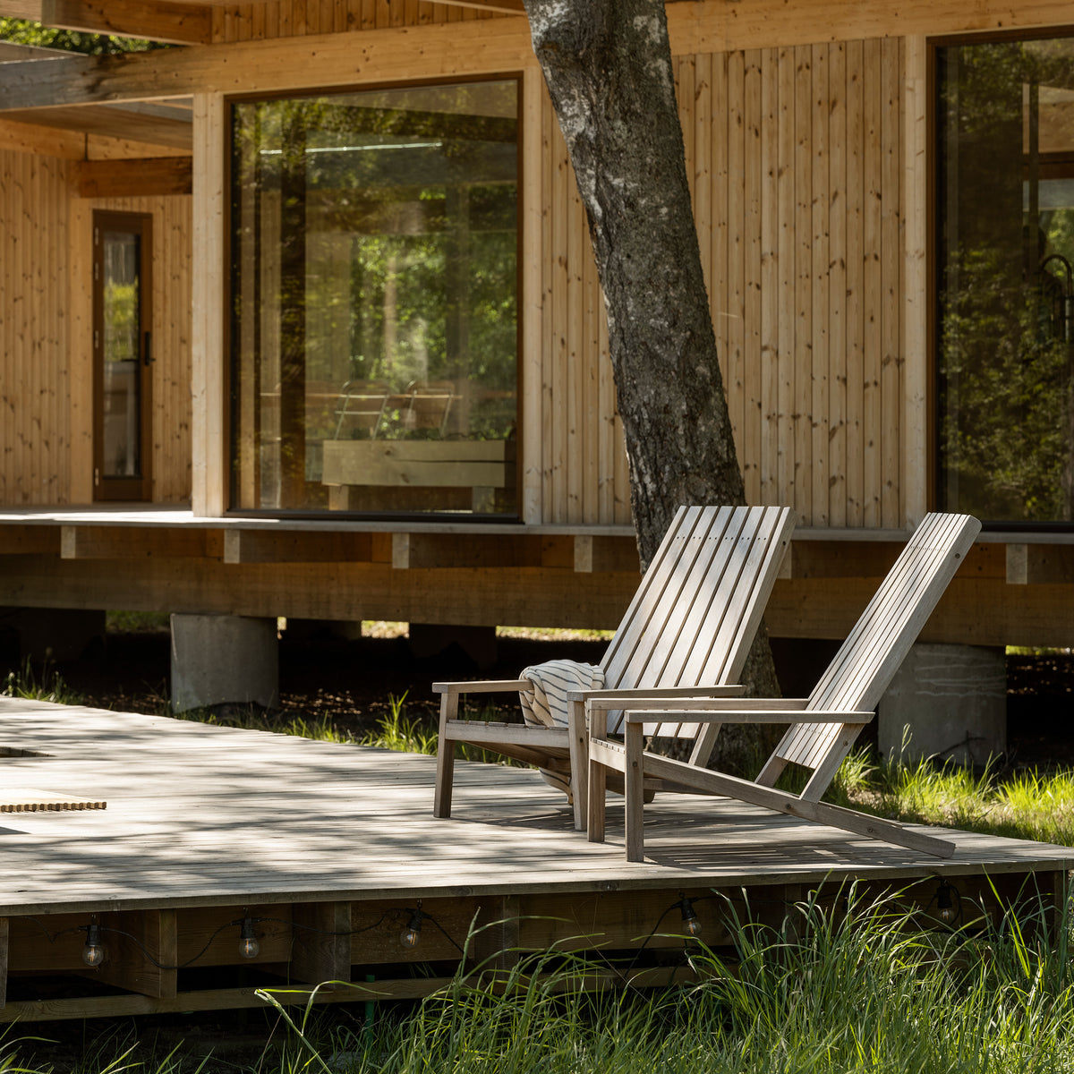 Fritz Hansen Between Lines Deck Chair by Stine Weigelt. Two wooden chairs sit on a sunny deck beside a tree.