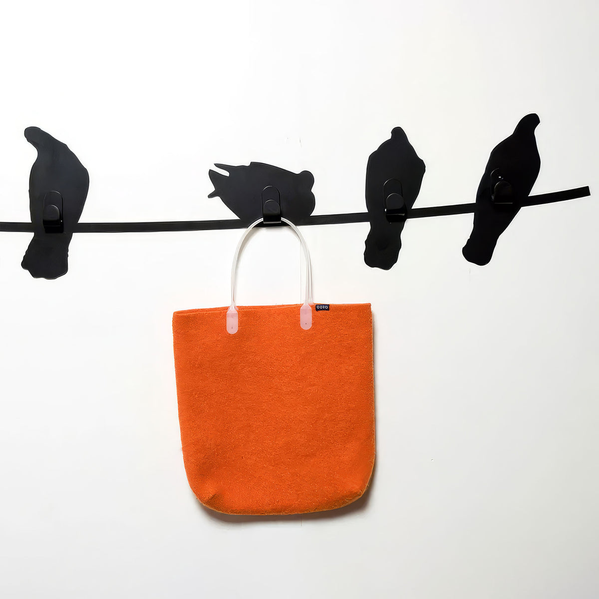 COVO Birds on Wire by Harry Allen. Four black birds perch on a line above a vibrant orange felt bag.