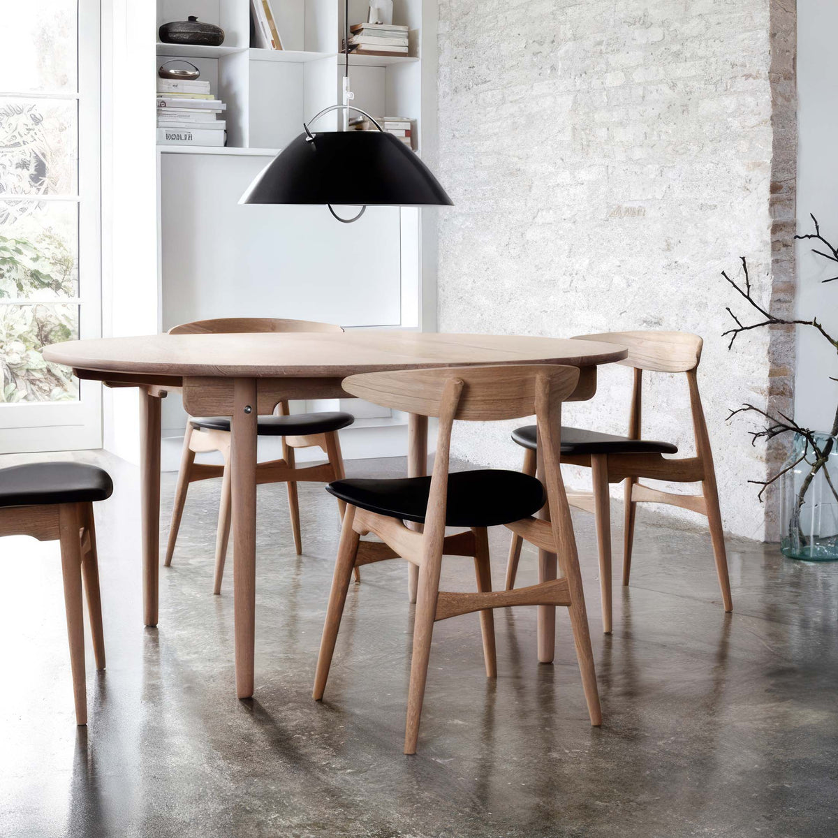 Carl Hansen & Søn CH33T Chair by Hans J. Wegner. A round wooden table with black-seated chairs in a minimalist dining room.