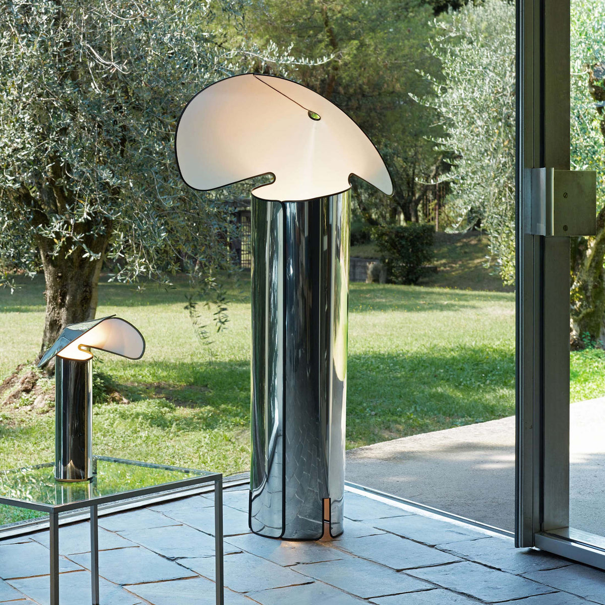 Flos Chiara Floor by Mario Bellini. A polished chrome mushroom-shaped lamp stands elegantly on a terrace.