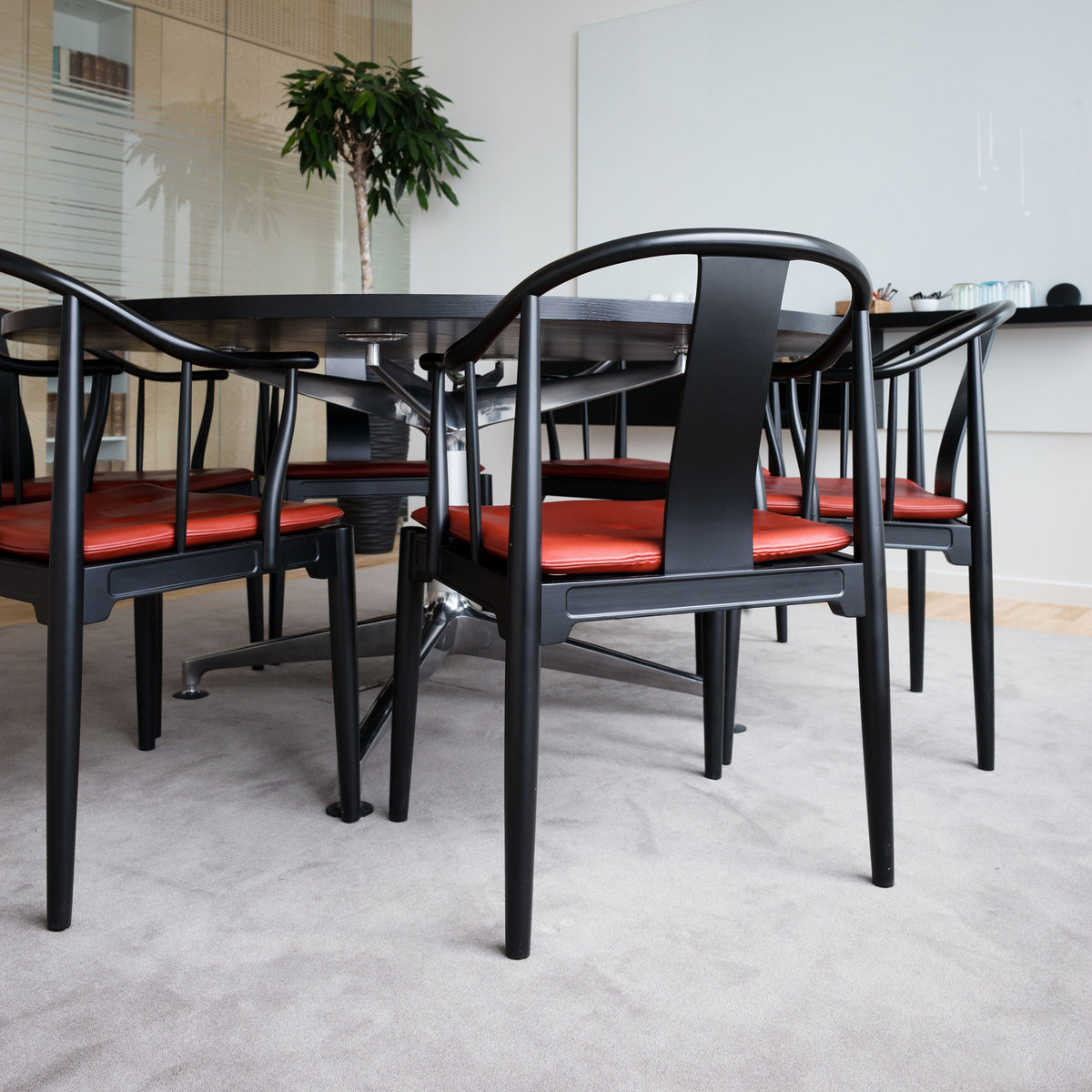Fritz Hansen China Chair™ by Hans J. Wegner. Black chairs with red cushions arranged around a table.