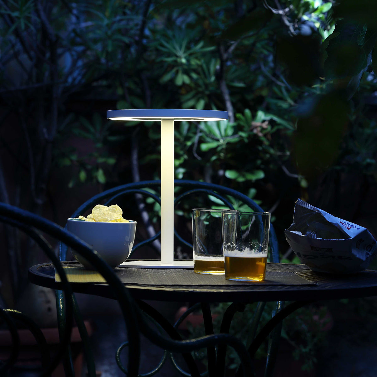 COVO Edvige by Enzo Calabrese. A minimalist white lamp illuminates an evening garden table with drinks and snacks.