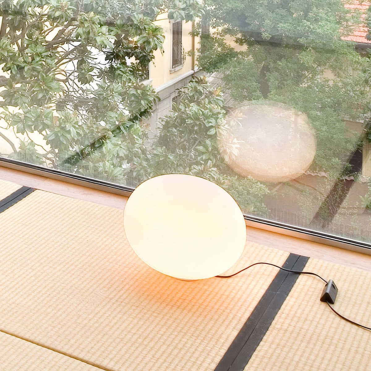 Flos Glo-Ball Basic 1 by Jasper Morrison. A glowing white spherical lamp sits on woven tatami matting indoors.