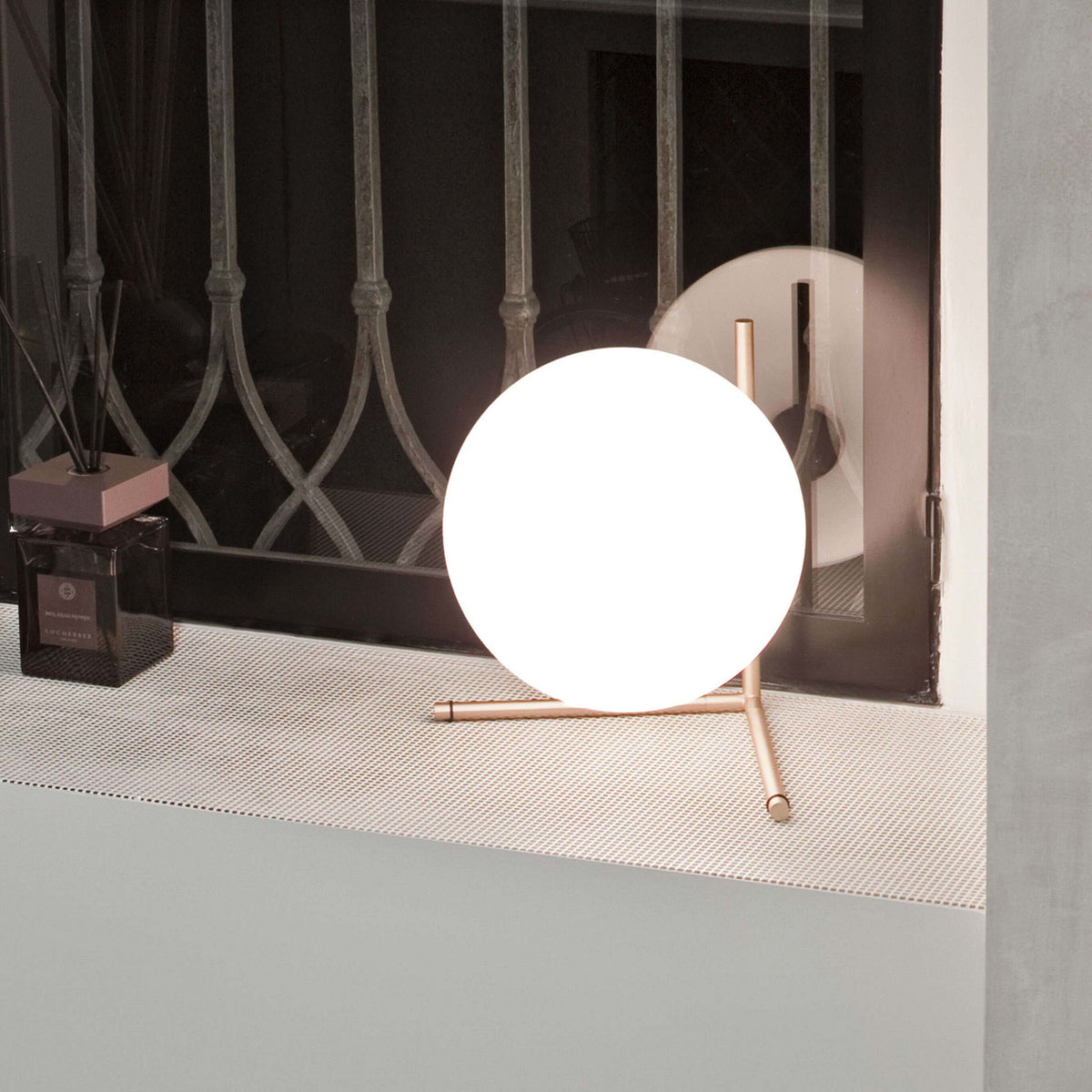 Flos IC Lights T2 by Michael Anastassiades. A glowing white sphere on copper tripod legs illuminates a modern interior space.