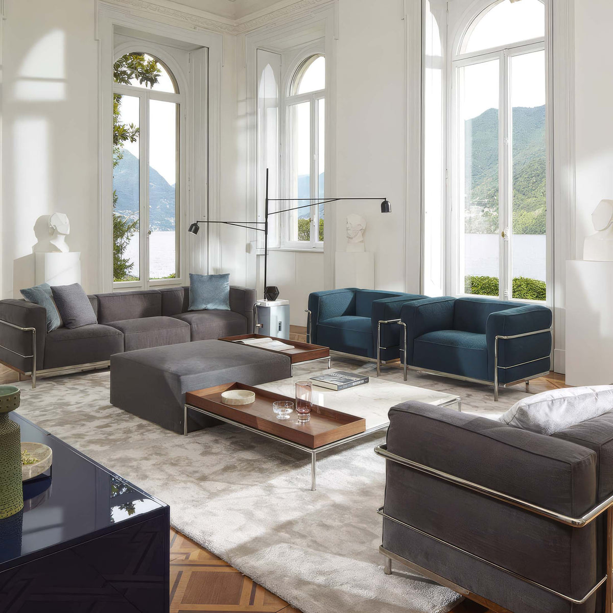 Cassina LC3 3 Seat Sofa by Le Corbusier. Modern sofas in charcoal and navy with metal frames in a bright lakeside room.