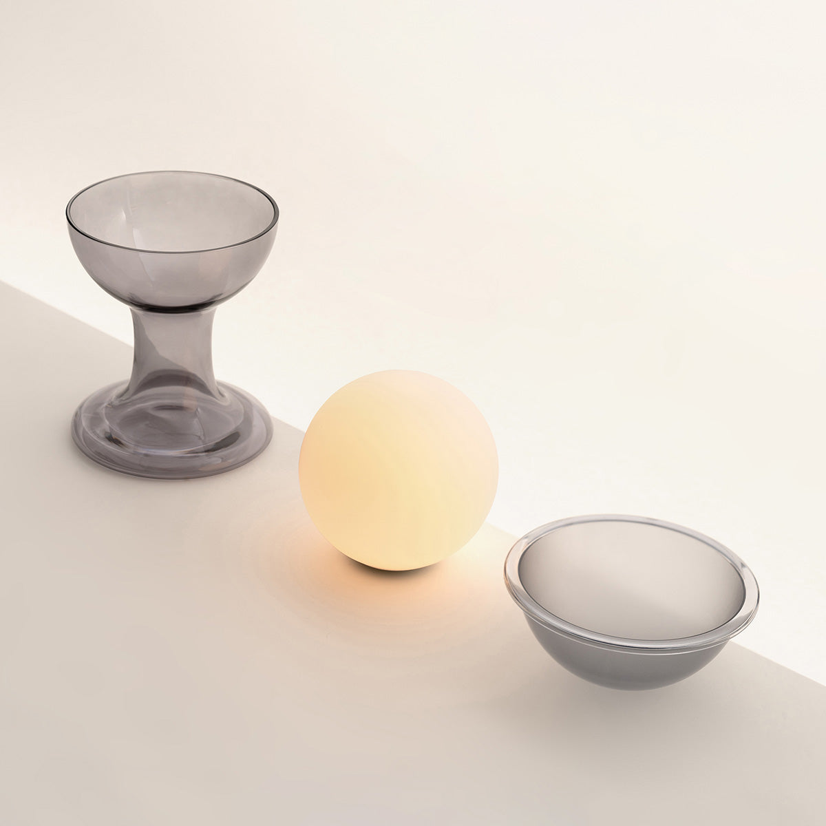 Established & Sons Gelato Lamp by Carlo Nason. A glowing sphere sits between two translucent gray vessels on a pale surface.