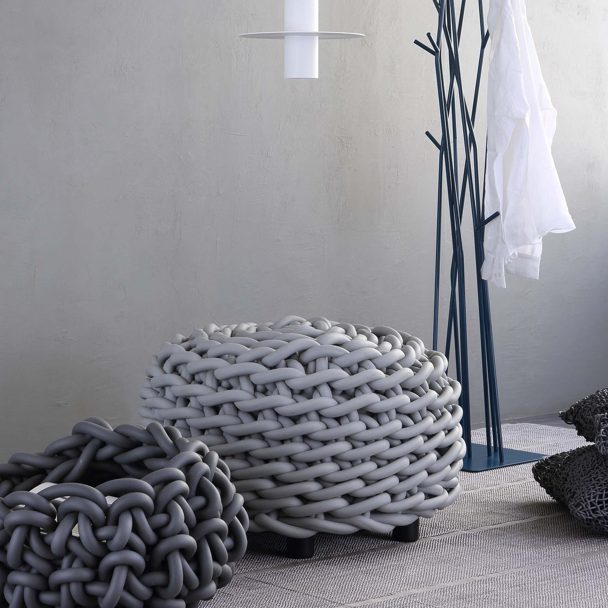 COVO Rebels 2 Pouf by Rosanna Contadini. A chunky braided rope basket sits on a textured gray rug in a minimalist white room.