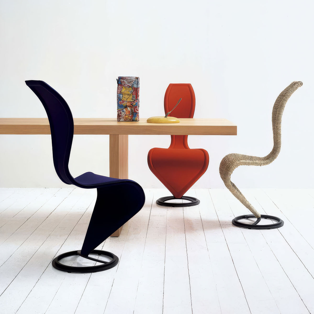 Cappellini S Chair by Tom Dixon. Three sculptural chairs in bold colors surround a wooden table with decorative objects.