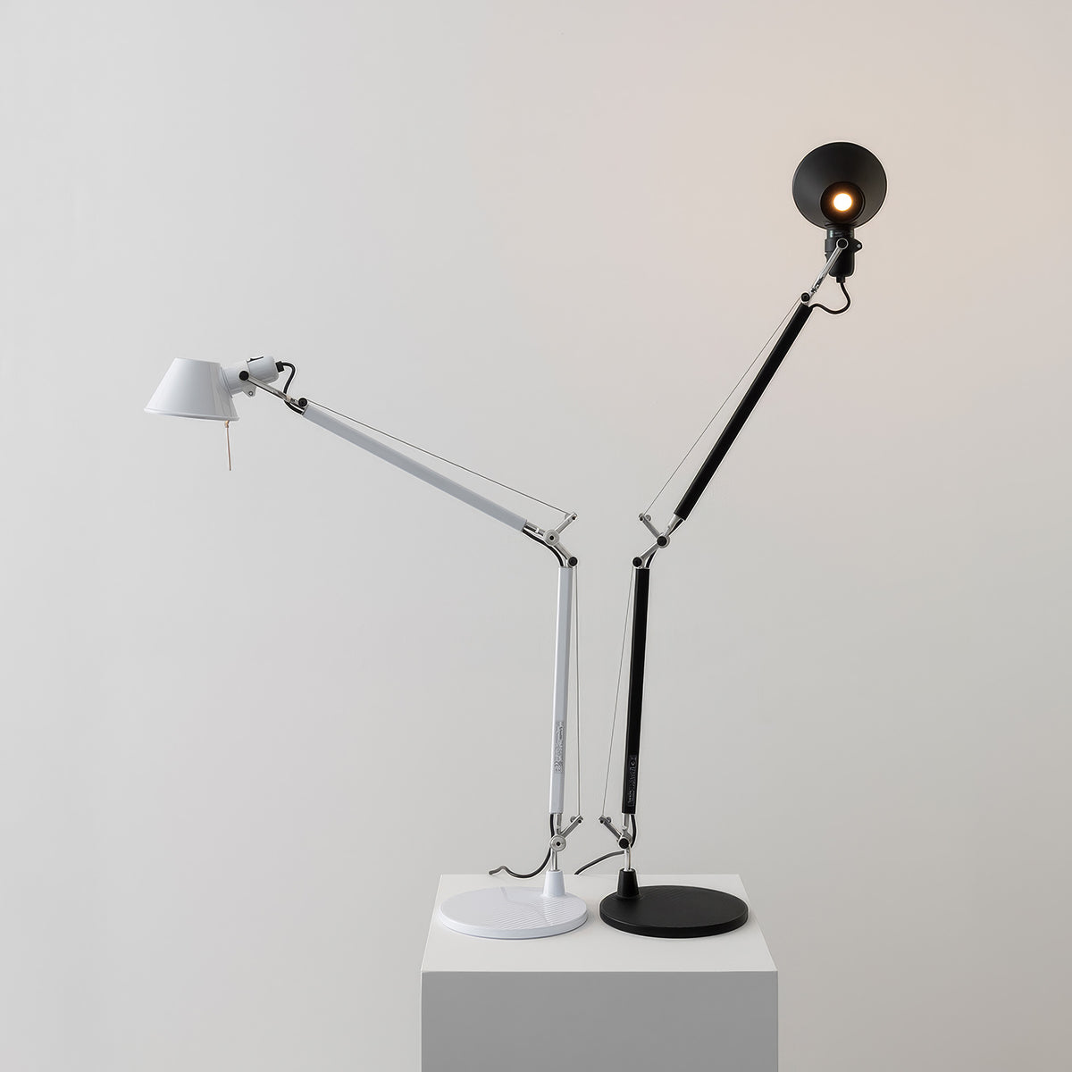 Artemide Tolomeo Table by Michele De Lucchi. Two articulated desk lamps in white and black stand on a gray cube.