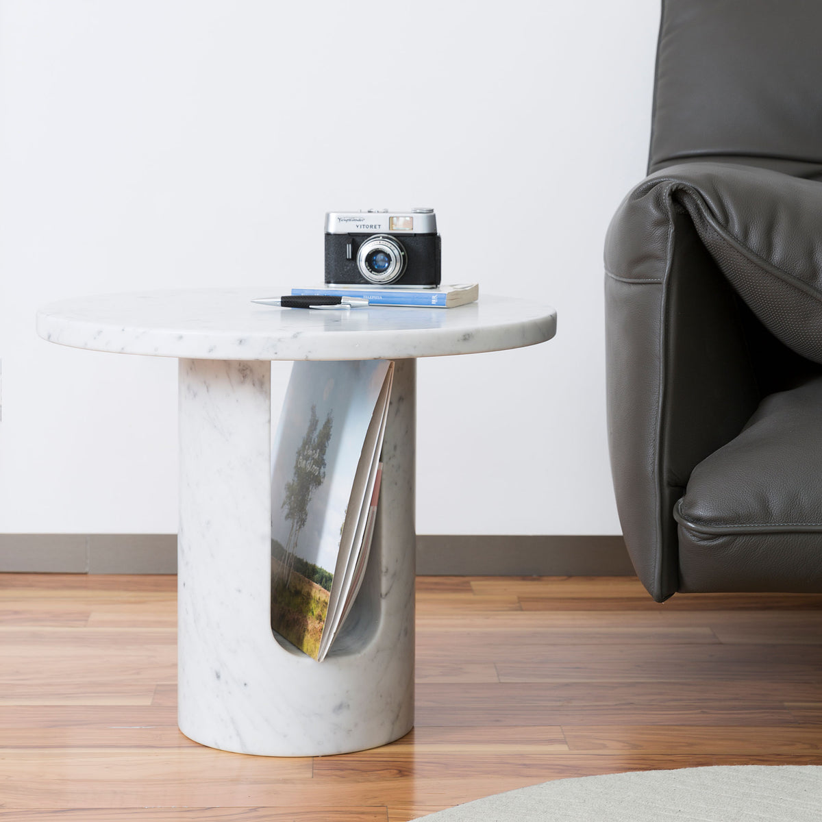 COVO U-TURN Table by Mikko Laakkonen. A marble side table holds a vintage camera, pen, and notebook beside a leather chair.