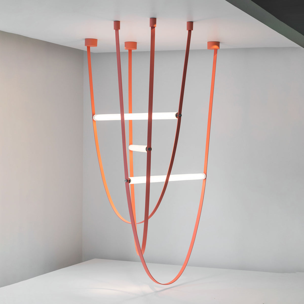 Flos Wireline by Formafantasma. Red and orange curved tubes with white shelves hang from a ceiling.