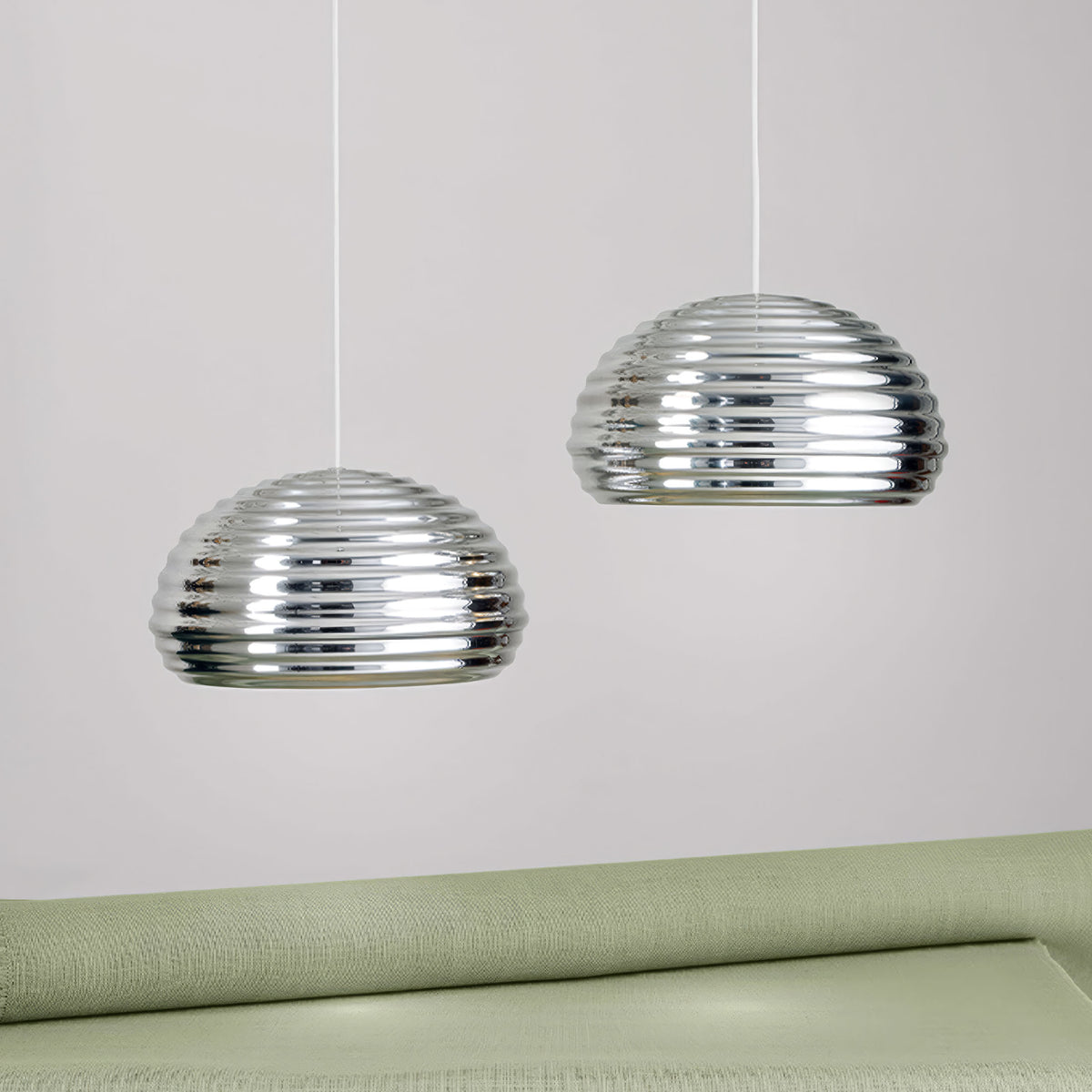Flos Splügen Bräu by Achille Castiglioni. Two reflective glass pendant lights hang above a pale green upholstered surface.