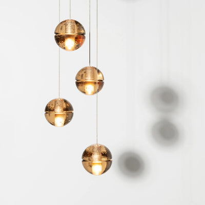 Bocci 14.20 Random by Omer Arbel. Four golden spheres with textured surfaces hang vertically, glowing warmly.