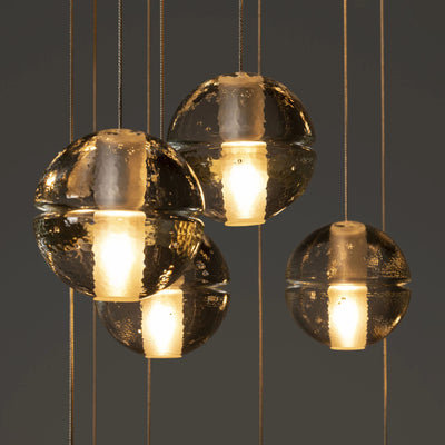 Bocci 14.36 Random by Omer Arbel. Golden spherical pendants with textured surfaces emit warm light against a gray backdrop.
