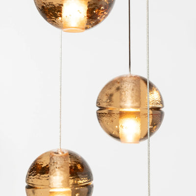 Bocci 14.36 Random by Omer Arbel. Three golden sphere pendant lights with textured finishes hang against a white background.