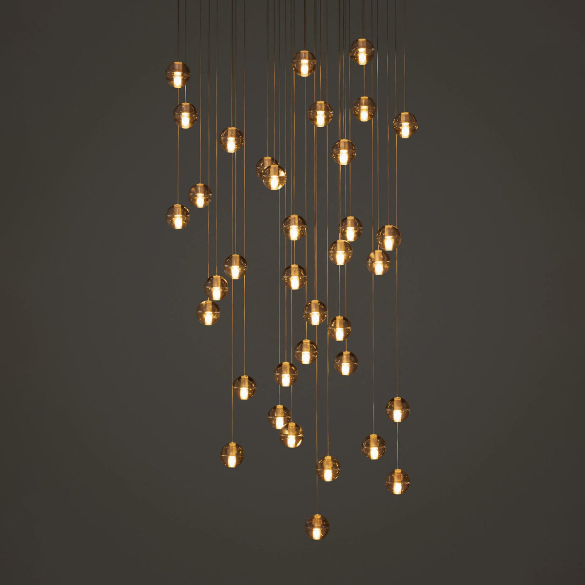 Bocci 14.36 Random by Omer Arbel. Multiple amber glass pendant lights hang at varying heights from thin wires.