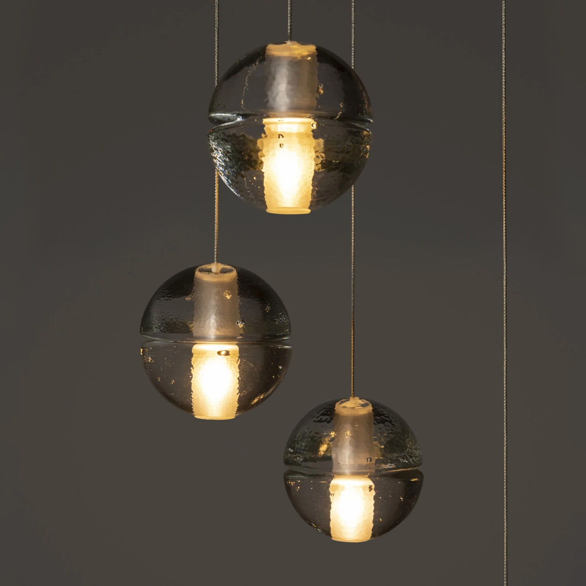 Bocci 14.5 Random by Omer Arbel. Three black spherical pendants with hammered surfaces emit warm golden light.