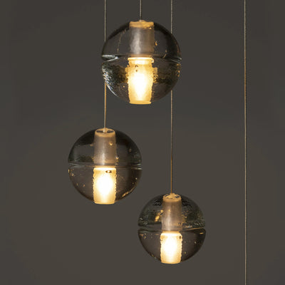 Bocci 14.5 Random by Omer Arbel. Three black spherical pendants with hammered surfaces emit warm golden light.