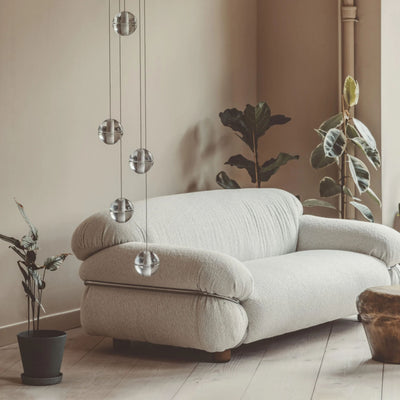 Bocci 14.5 Random by Omer Arbel. A plush cream sofa sits in a minimalist room with hanging glass orbs and potted plants.