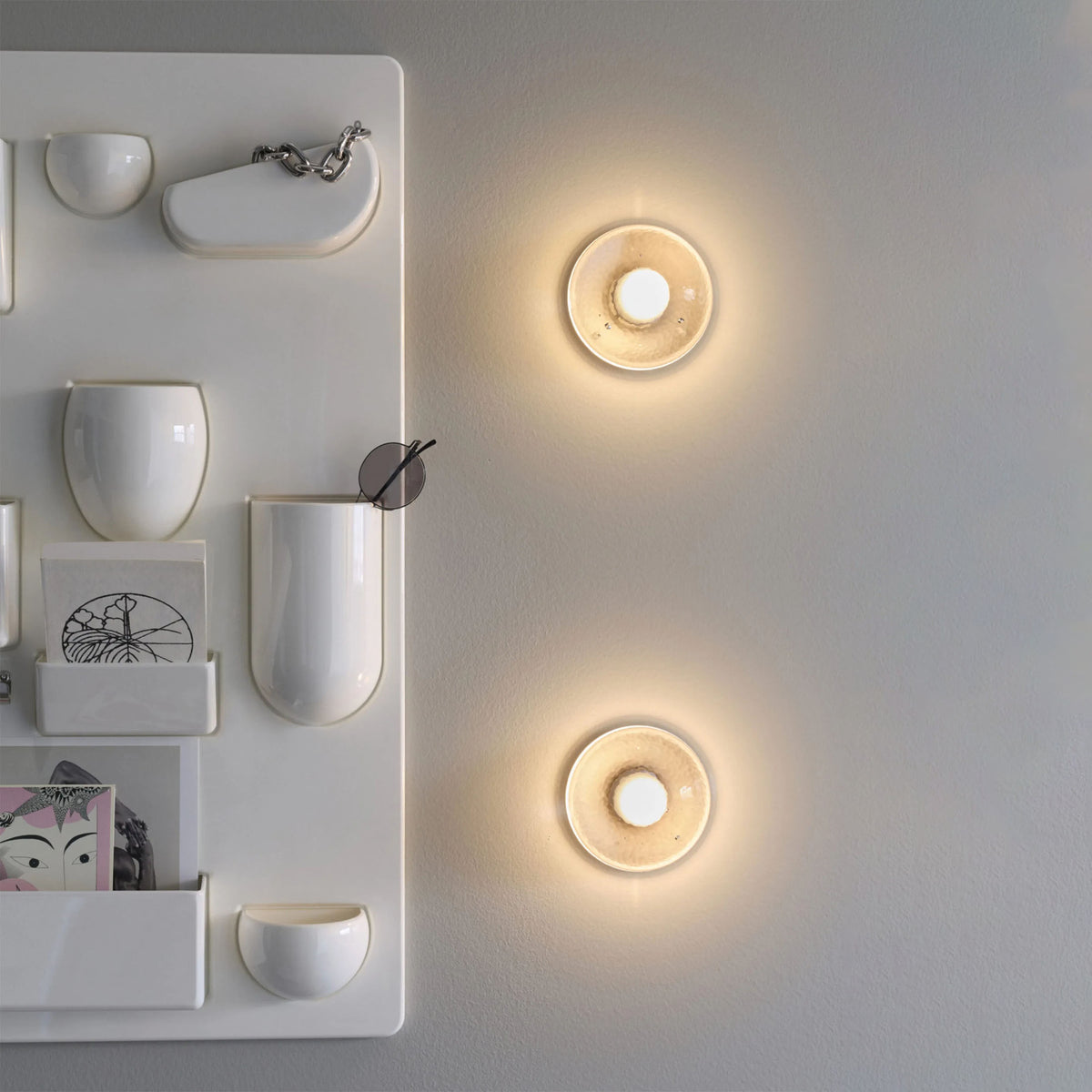 Bocci 14s Wall and Ceiling Lamp by Omer Arbel. Warm wooden circular wall lights glow softly above minimalist white shelving.