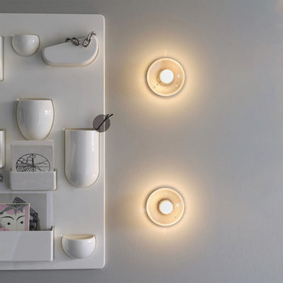 Bocci 14s Wall and Ceiling Lamp by Omer Arbel. Warm wooden circular wall lights glow softly above minimalist white shelving.