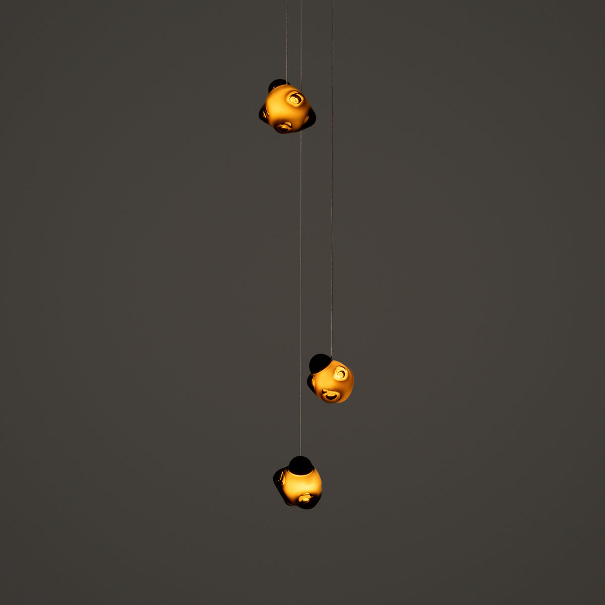 Bocci 57.3 Random by Omer Arbel. Three golden spherical lights hang vertically against a gray wall.