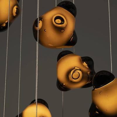 Bocci 57.5 Random by Omer Arbel. Golden spheres with black accents hang from silver strings against a gray backdrop.