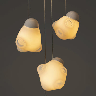 Bocci 57.5 Random by Omer Arbel. Three warm yellow pendant lights with gray caps hang against a dark background.
