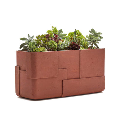 Indigenus Aarde by Sebastian Herkner. A terracotta concrete planter filled with vibrant green and burgundy succulents.