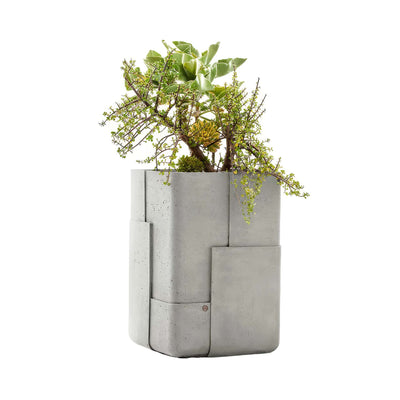 Indigenus Aarde by Sebastian Herkner. A concrete planter with geometric panels holds succulents and trailing green plants.