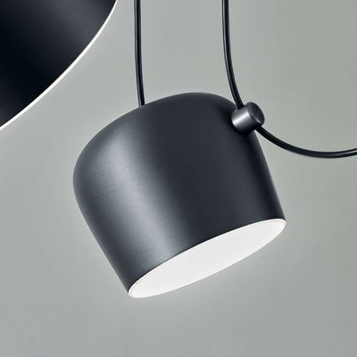 Flos Aim Suspension Lamps by Erwan & Ronan Bouroullec. A sleek black pendant lamp with white interior glows softly.