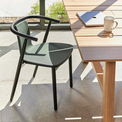 Cappellini Bac Chair by Jasper Morrison. A modern black chair with green upholstery sits at a wooden table in sunlit space.