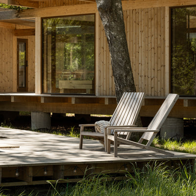Fritz Hansen Between Lines Deck Chair by Stine Weigelt. Two wooden chairs sit on a sunny deck beside a tree.