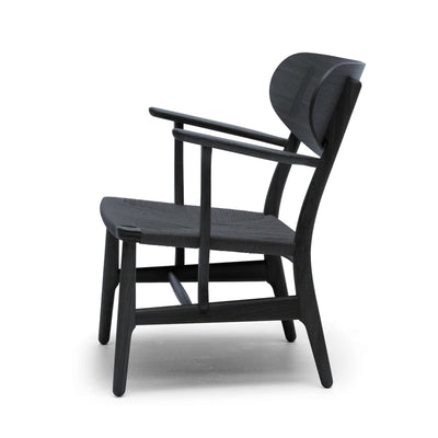 Carl Hansen & Søn CH22 Lounge Chair by Hans J. Wegner. A black wooden chair with woven seat and back.
