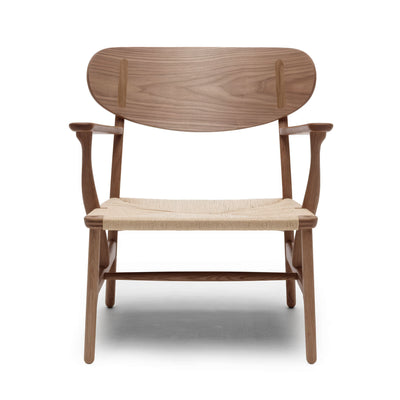 Carl Hansen & Søn CH22 Lounge Chair by Hans J. Wegner. Wooden chair with woven seat and curved backrest.