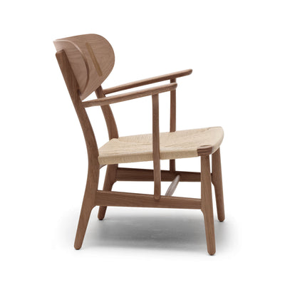 Carl Hansen & Søn CH22 Lounge Chair by Hans J. Wegner. A wooden chair with a woven seat and curved backrest.