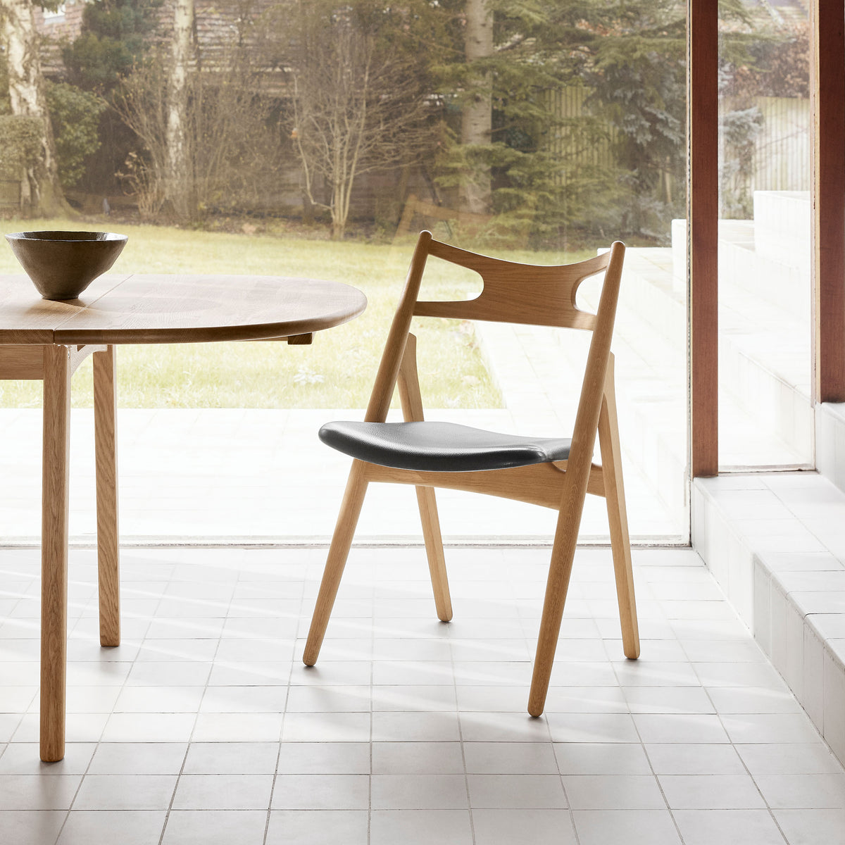 Carl Hansen & Søn CH29P Sawbuck Chair by Hans J. Wegner. Natural wood chair with black seat in bright room.