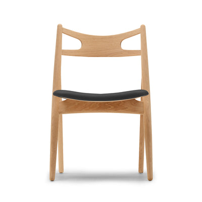 Carl Hansen & Søn CH29P Sawbuck Chair by Hans J. Wegner. A natural wood chair with a black seat cushion.