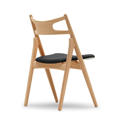Carl Hansen & Søn CH29P Sawbuck Chair by Hans J. Wegner. Natural wood frame chair with black seat cushion.