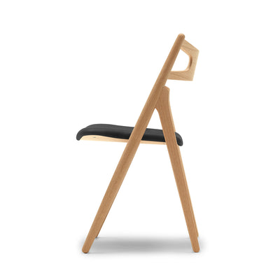 Carl Hansen & Søn CH29P Sawbuck Chair by Hans J. Wegner. Natural wood frame with black padded seat.