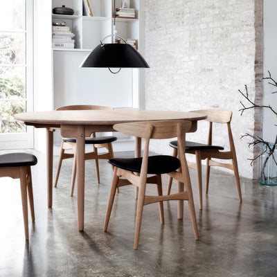 Carl Hansen & Søn CH33T Chair by Hans J. Wegner. A round wooden table with black-seated chairs in a minimalist dining room.