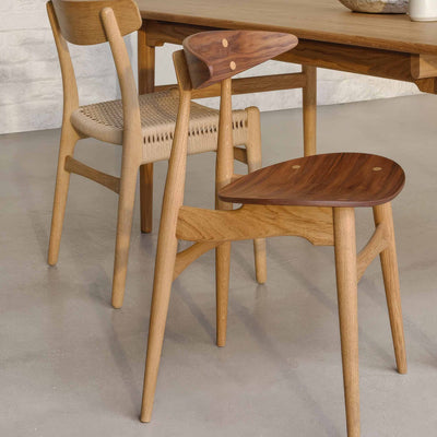 Carl Hansen & Søn CH33T Chair by Hans J. Wegner. Wooden chairs with woven and solid seats surround a table.