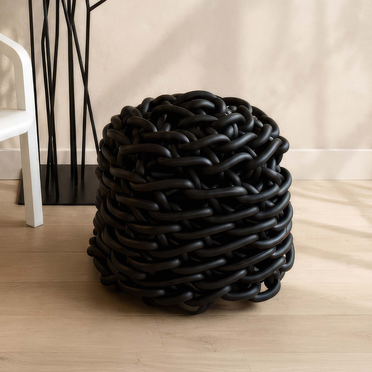 COVO Colosso pouf by Rosanna Contadini. A sculptural black object with interwoven tubular forms sits on wooden flooring.
