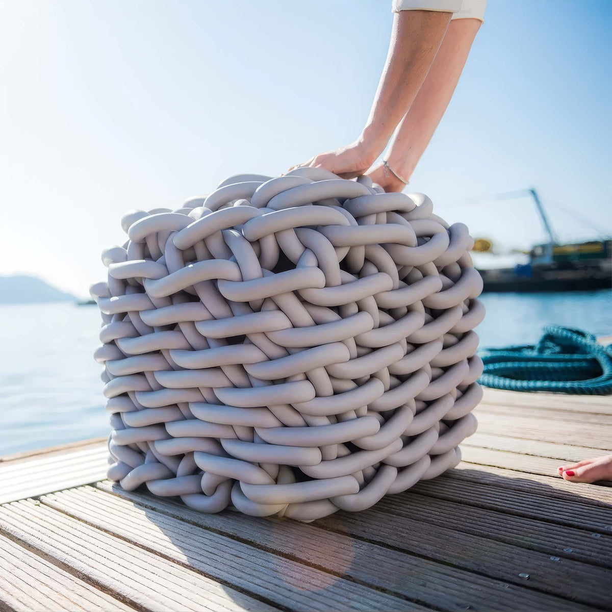 COVO Colosso pouf by Rosanna Contadini. A hand rests on a thick coiled rope at a seaside dock.
